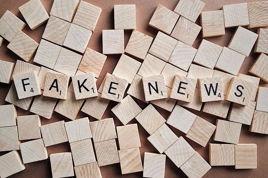 Scrabble tiles on a wooden surface spell "FAKE NEWS" amid scattered empty wooden cubes.