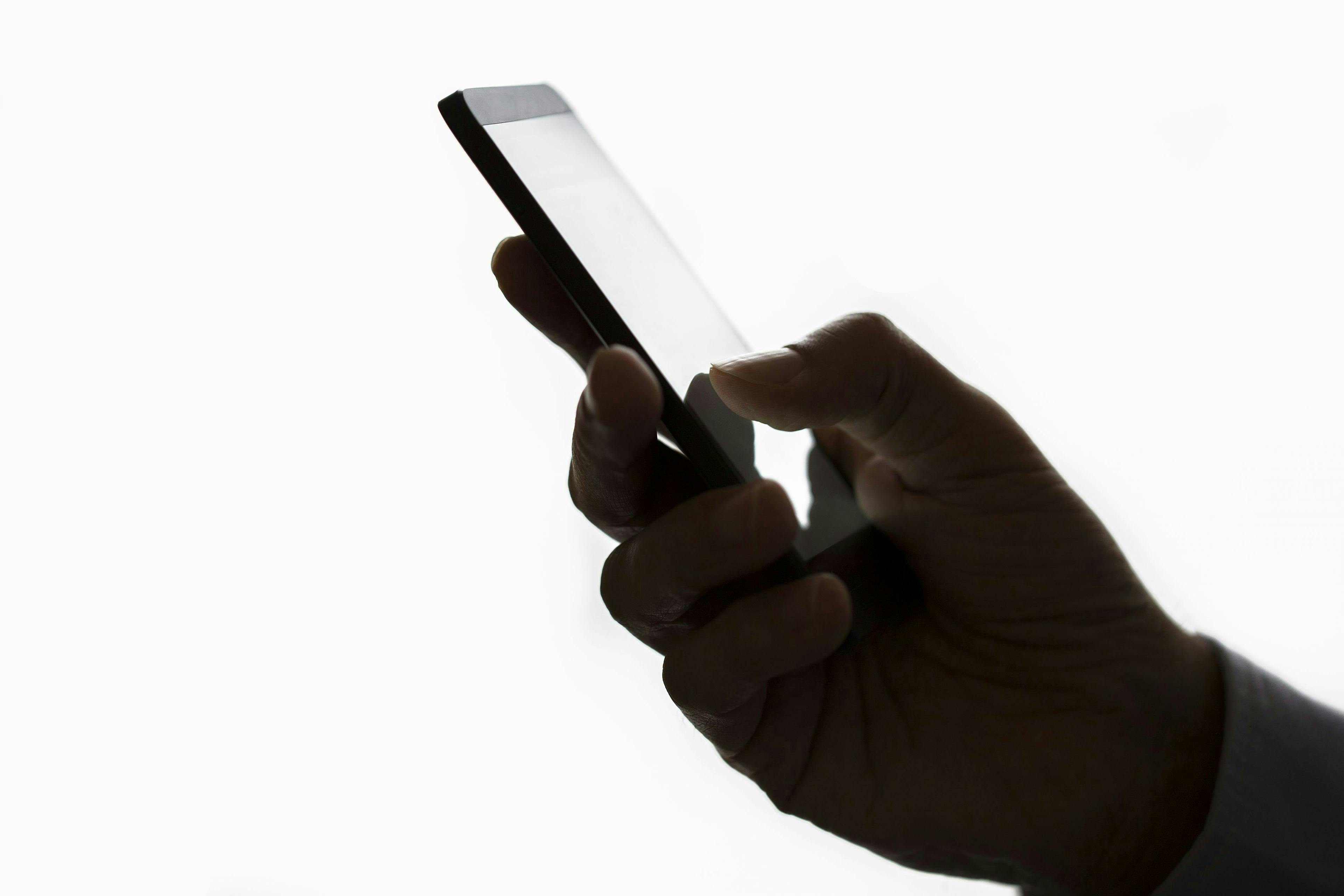 A hand holds a smartphone with fingers touching the screen, against a plain white background.