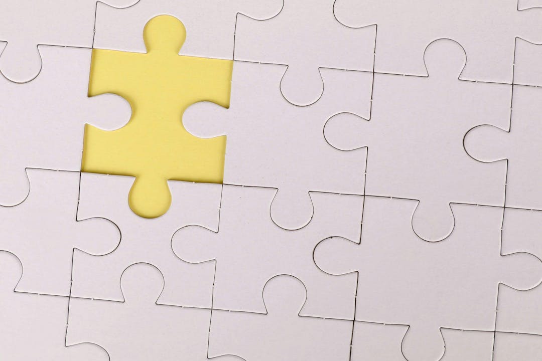 A white puzzle piece rests in place, surrounded by other pieces, with one piece missing, revealing a yellow background beneath.