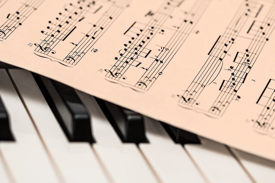 A sheet of music notation rests on the black and white keys of a piano, suggesting a scene of musical practice or performance.