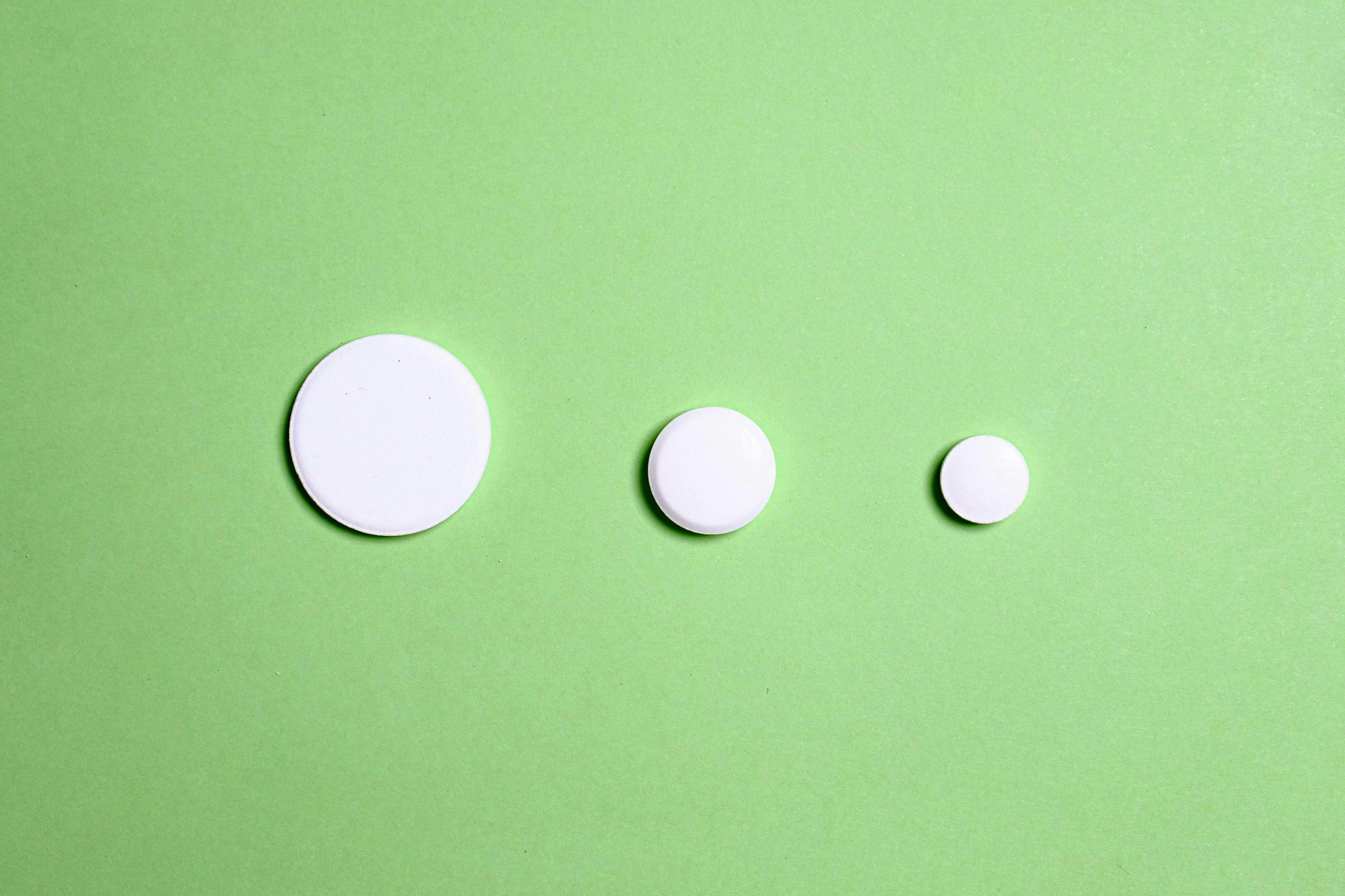 Three white, round, flat objects of varying sizes are arranged in a rightward diagonal line on a light green background.