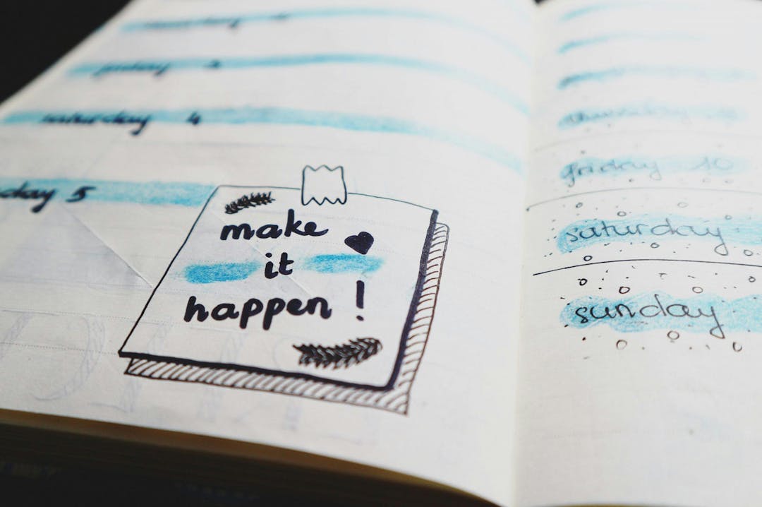 Notebook featuring handwritten pages with days of the week highlighted in blue, accompanied by a motivational note reading "make it happen!" with decorative elements.