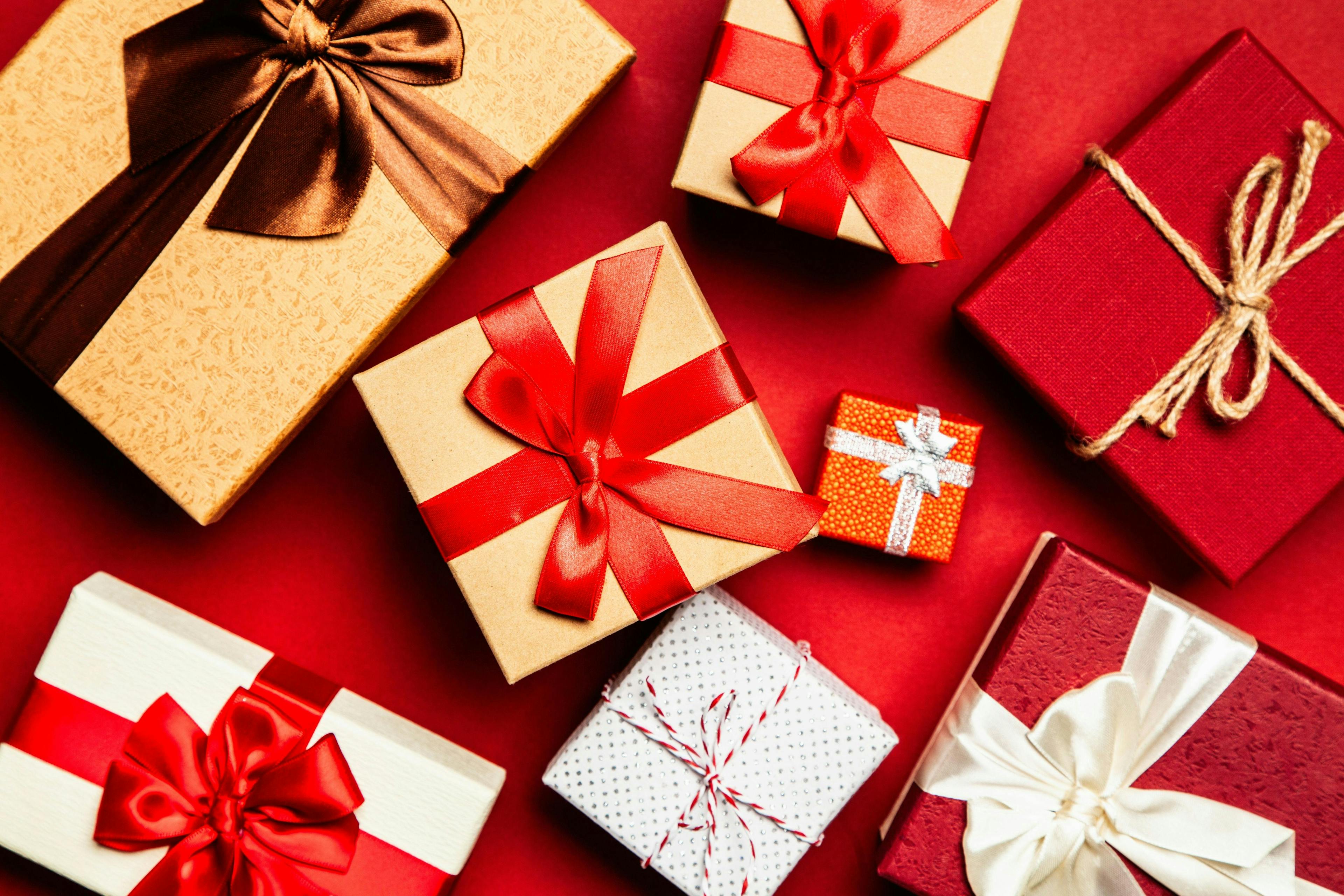 Gift boxes wrapped in various papers with colorful ribbons, arranged together on a red background.