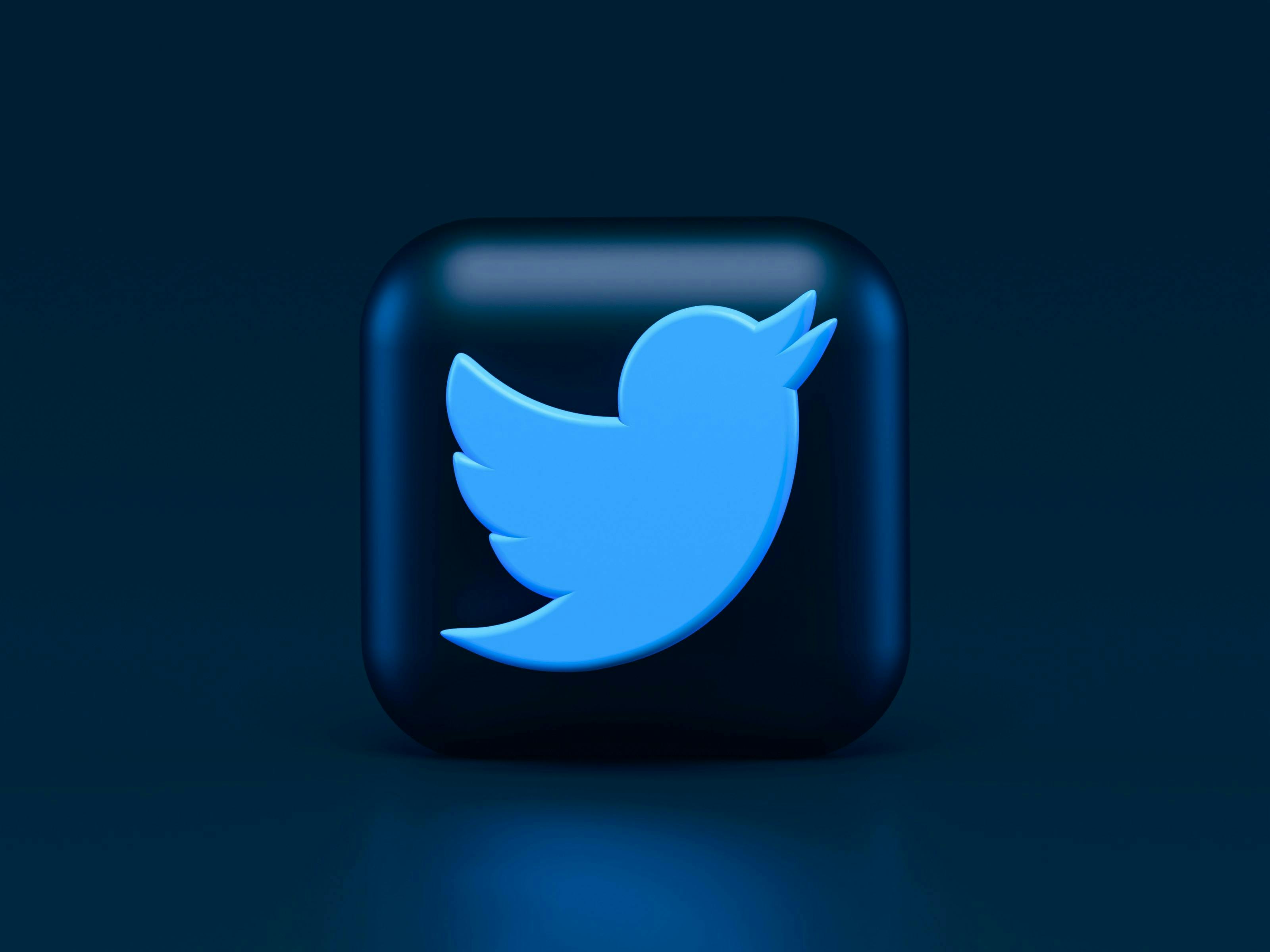 A blue bird icon is centered on a rounded black square, set against a dark blue background, representing the Twitter logo. No text is present.