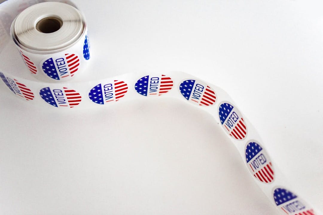 A roll of "I VOTED" stickers with an American flag design, unfurled partially, on a white background.