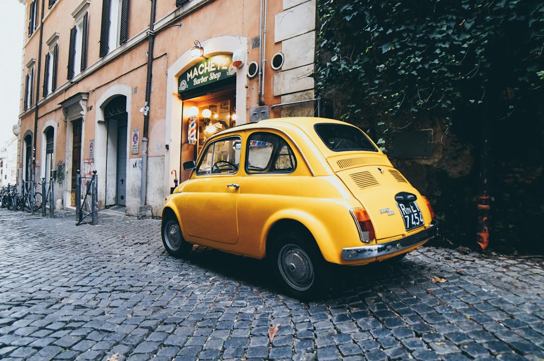 An old-fashioned yellow car parked in a street in Rome
