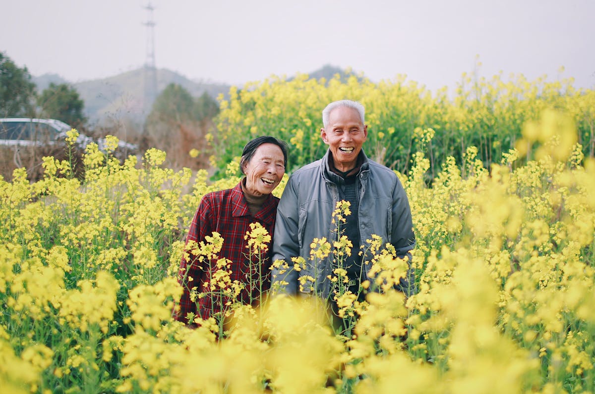 Two older adults smiling and standing in a field of flowers.