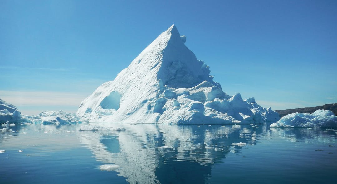 A pyramid-shaping iceberg surrounded by deep blue water.