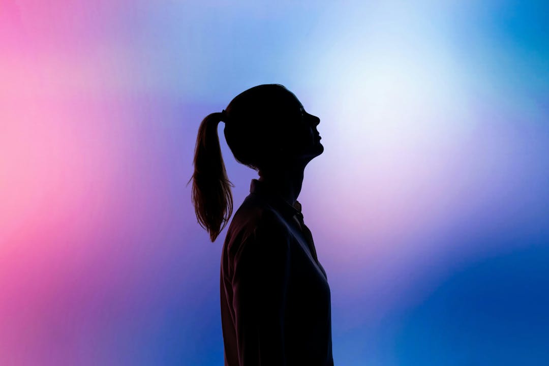 The silhouette of a woman in front of a pink and blue background.