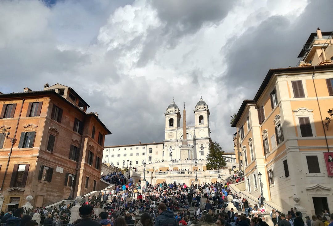 A large number of people walking through the city of Rome with buildings and a church